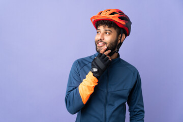Young Moroccan cyclist man isolated on purple background looking up while smiling