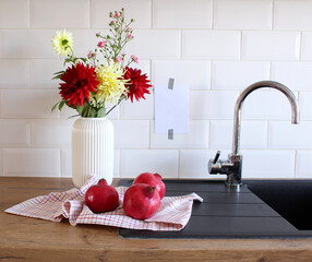 Modern kitchen still life. Blank paper card mock-up taped on white tiles wall. Dahlias flowers and roses branches in a white vase. Home concept.