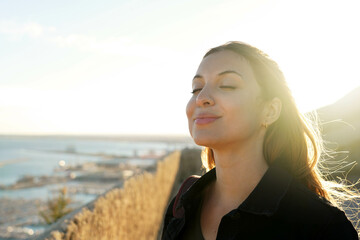 Beautiful young woman with closed eyes breathing with wind on her face relaxing enjoying sun at...