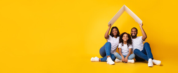 Happy African American parents holding cardboard roof above daughter, panorama