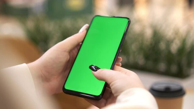 Shopping center. Back view of brunette holding chroma key green screen smartphone watching content. Shopping online. Gadgets and contemporary people concept.