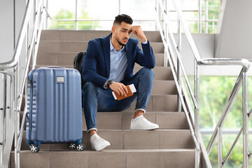 Upset Middle Eastern Guy Sitting On Airport Terminal Stairs With Luggage