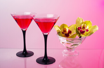 Two glasses with a cocktail, two orchids in a vase on a glass table.