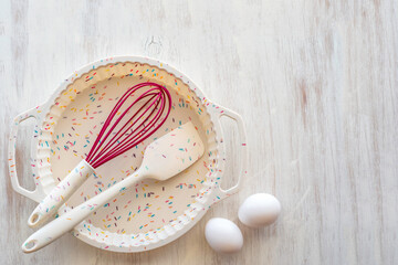 Silicone cake form, spatula and whisk on white wooden background.