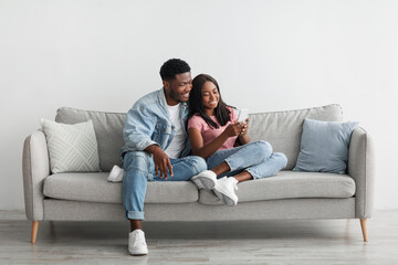 Obraz premium African american couple sitting on couch, sharing using cellphone