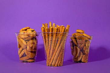 Plastic cup with a background. Plastic cups and crackers. Sweet pretzel. Snack serving containers. Full plastic cup on colored background. Food in a clear glass