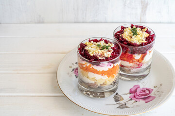 Dressed Herring or Herring Under Fur Coat in glasses on vintage plate over wooden background. Traditional Russian salad with herring fillets boiled potatoes, carrots, beets and mayonnaise.