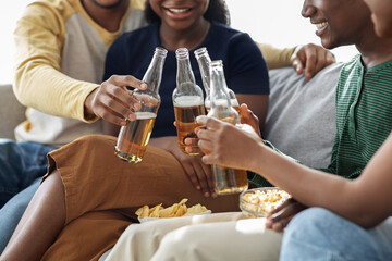 Unrecognizable black friends cheering with bottles of beer, closeup
