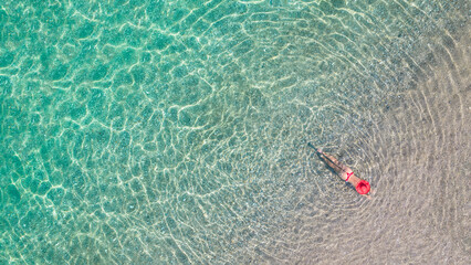 Top view. Young beautiful woman in a red hat and bikini lying and sunbathe in sea water on the sand beach. Drone, copter photo. Summer vacation. View from above.