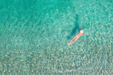 Obraz premium Top, aerial view. Young beautiful woman in a hat and white bikini swimming in sea water on the sand beach. Drone, copter photo. Summer vacation. View from above.