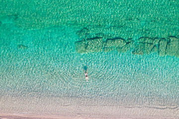 Top, aerial view. Young beautiful woman in a hat and white bikini swimming in sea water on the sand beach. Drone, copter photo. Summer vacation. View from above.