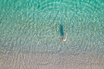 Top view. Young beautiful naked woman in a hat taking off bikini in sea water. Drone, copter photo. Summer vacation. View from above.
