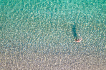 Top view. Young beautiful naked woman in a hat taking off bikini in sea water. Drone, copter photo....