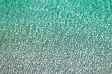 Background, texture of relaxing, calm turquoise, transparent sea water with stones. Summer vacation. Blue ocean lagoon. Drone, copter top view.