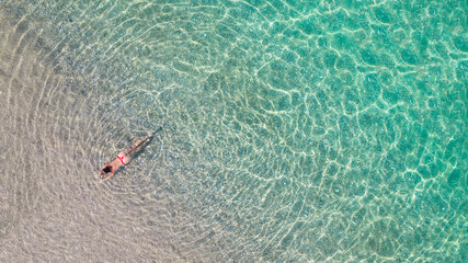 Top, aerial view. Young beautiful woman in a red bikini panties lying and sunbathe in sea water on the sand beach. Drone, copter photo. Summer vacation. View from above.