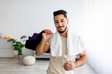 Handsome young Arab guy holding bottle of water and sports bag, posing after domestic training...