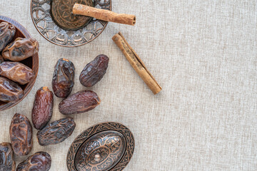 Dried date fruits, cinnamon sticks, stylized Arabic crockery for Ramadan on cotton fabric background with copy space.