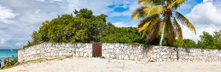 Isla Catalina, eine Insel der Dominikanischen Republik in der Karibik. Eine Mauer aus Steinen am Strand, Palmen und ein blauer Himmel als Panorama. © AIDAsign