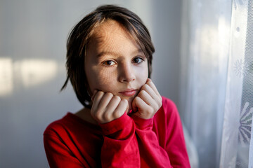 Artistic portrait of a teenage boy, standing next to a window, shadows from curtains falling on his face, making interesting shadows