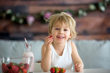 Cute toddler child, blond boy, drinking smoothie and easting strawberries
