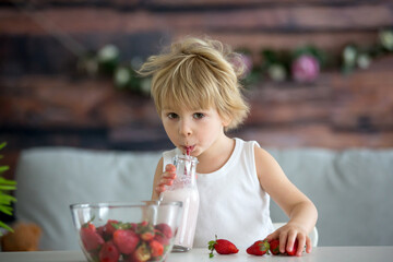 Cute toddler child, blond boy, drinking smoothie and easting strawberries