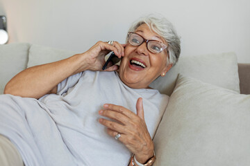 Senior woman has a happy conversation at cellphone. Smiling senior woman using phone sitting on couch at home. Shot of a senior woman talking on mobile phone while sitting in her room. Copy space.