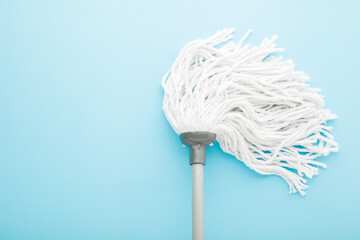 New white mop head with stick on light blue background. Pastel color. Closeup. Cleaning tool for...