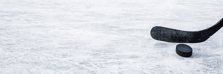 Old black hockey stick and rubber puck on ice background. Closeup. Wide banner. Empty place for...