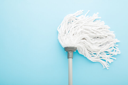 New white mop head with stick on light blue background. Pastel color. Closeup. Cleaning tool for different floor washing. Empty place for text. Top down view.