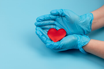 Fototapeta premium Red heart in hands in blue medical gloves on blue background. Background for the day of the medic. World Heart Day. Heart diseases.