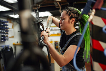 Obraz na płótnie Canvas Concentrated woman fixing bike wheel in workshop