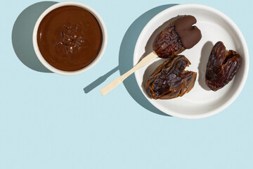 Plate with chocolate dipped dried date fruits in the form of heart on blue background with copy space.