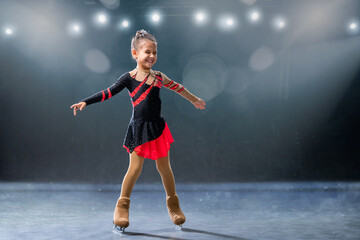 Fototapeta na wymiar Little skater rides on rings in red and black dress on ice arena