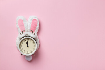 Alarm clock in easter bunny ears on a pink background with copy space.