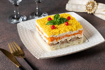 Traditional Russian puff salad Mimosa with canned fish, potatoes, cheese, carrots and eggs on brown background