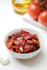 Sun dried tomatoes  on white bowl, white wooden background. Dried tomatoes with olive oil, salt, herbs and garlic recipe.  Top view,  copyspace.