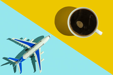 Decorative passenger plane and cup of coffee on blue and yellow background. Holiday concept.