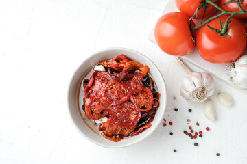 Sun dried tomatoes  on white bowl, white wooden background. Dried tomatoes with olive oil, salt, herbs and garlic recipe.  Top view,  copyspace.