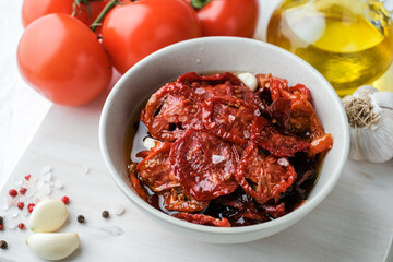 Sun dried tomatoes  on white bowl, white wooden background. Dried tomatoes with olive oil, salt, herbs and garlic recipe.  Top view,  copyspace.