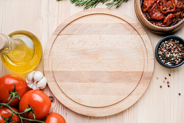 Empty round cutting board  with copyspace. Decorated with oil, tomatoes, pepper, rosemary, garlic on light wooden background. Top view.