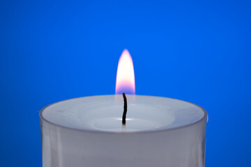 Single small white candle burning. Close up studio shot, isolated on blue background