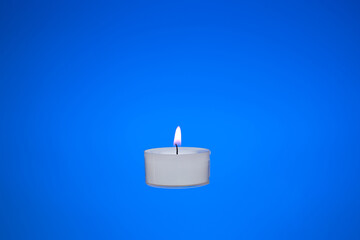 Obraz na płótnie Canvas Single small white candle burning. Close up studio shot, isolated on blue background