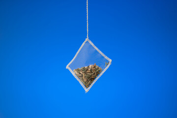Transparent square tea bag with dried fruits and ground leafs. Close up studio shot, isolated on blue background, no people