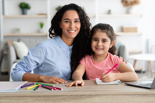 Happy Mother And Little Daughter Posing At Table While Making Homework Together