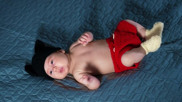 Caucasian little kid wearing costume of Mickey Mouse on bed. Adorable kid in funny costume at the grey backdrop. Top view.