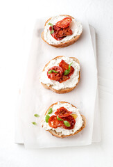 three bruschettas with ricotta cheese, olive and dried tomatoes on ciabatta bread on white background. Olive oil and spices decorated. top view