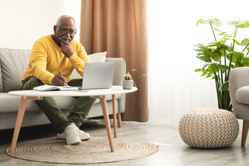 Senior Black Male Using Laptop Working Online Taking Notes Indoor
