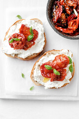 Two bruschettas with ricotta cheese, olive and dried tomatoes on ciabatta bread on white background. Olive oil and spices decorated. Copyspace.