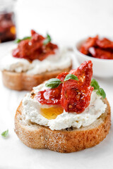 Two bruschettas with ricotta cheese, olive and dried tomatoes on ciabatta bread on white background. Olive oil and spices decorated. Copyspace.