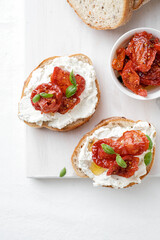 Two bruschettas with ricotta cheese, olive and dried tomatoes on ciabatta bread on white background. Olive oil and spices decorated. Copyspace.